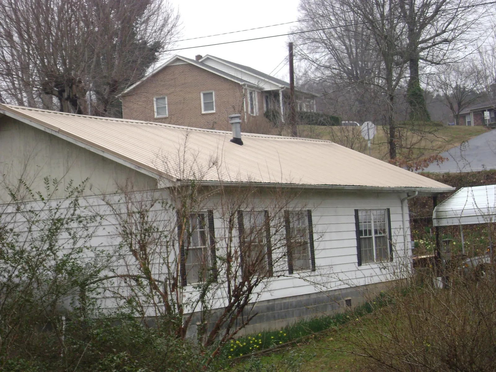 Tan metal roof on a white sided house set into a hillside — Commercial Roofing by Roofing Brothers in South Tamworth